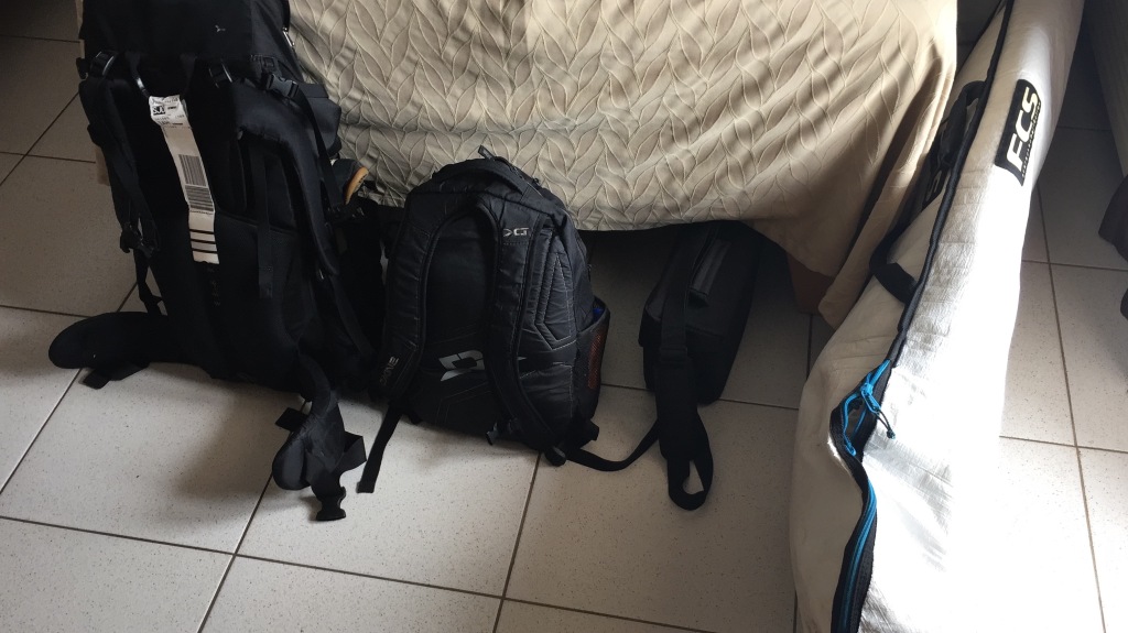 Two backpacks and a surfboard sit on the ground of a hotel room in Costa Rica.